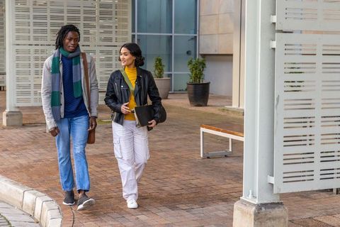 Diverse young adults walking and chatting on urban plaza holding tablet