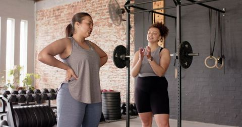 Multiracial women cheering while strength training in sunlit gym, workout partners