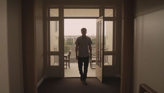 Backlit silhouette of man walking through double glass doors from balcony into corridor