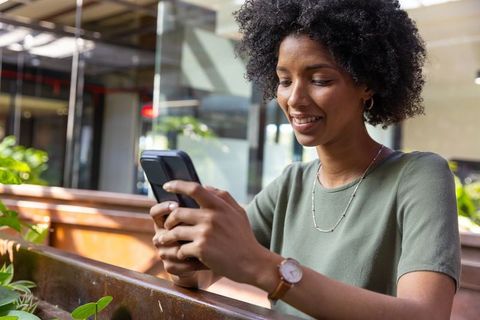 Smiling Woman Engaging with Smartphone in Urban Cafe Setting