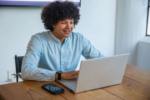 Smiling Professional Typing on Laptop Facing Large Window