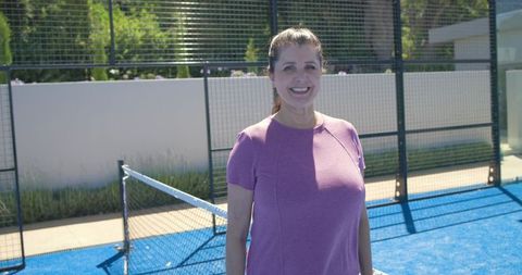 Mature woman smiling and standing on blue pickleball court wearing mauve active top