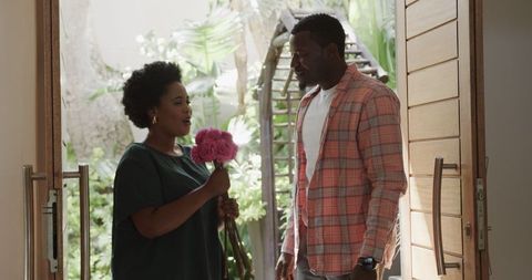 Friends Chatting Happily Indoors, Woman Holding Pink Flowers