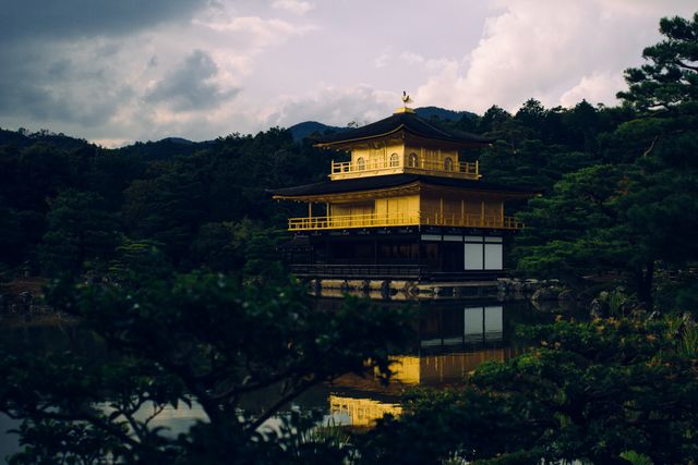 Golden Pavilion Temple, a famous historical and cultural landmark in Kyoto, reflected in a serene pond. Surrounded by lush greenery and under a cloudy sky, the scene exudes tranquility and connection to nature. Ideal for travel brochures, tourism websites, and cultural heritage promotions.