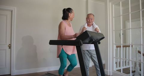Senior asian couple exercising together on home treadmill