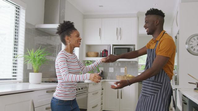 Happy African American couple dancing and enjoying themselves in a modern kitchen environment. Suitable for themes of love, relationship, companionship, domestic bliss, and joyful moments at home.