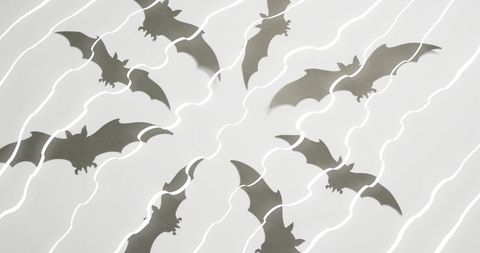 Paper bat silhouettes radiating on white surface with dramatic diagonal light streaks