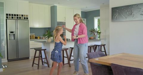 Mother and daughter dancing in modern kitchen sharing playful family moment