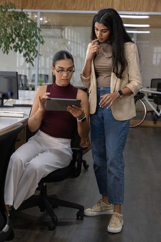 Multicultural female coworkers collaborating on tablet in modern minimalist office space