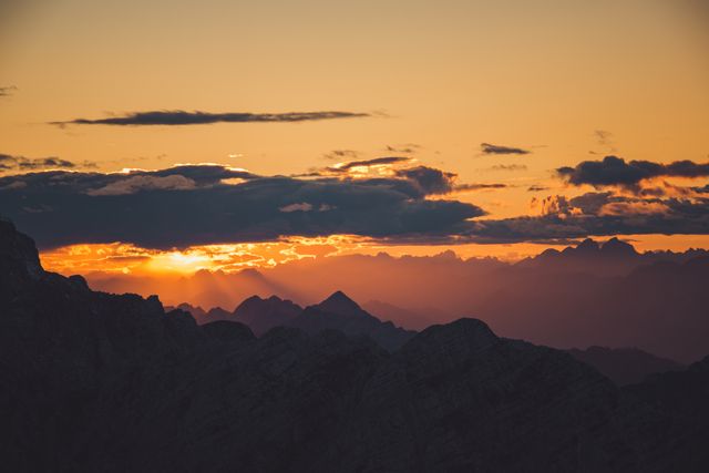 This image depicts a breathtaking view of a mountain range during sunset, with the dramatic sky casting vibrant colors across the horizon. Ideal for travel websites, nature blogs, or backgrounds for presentations showcasing the beauty of natural landscapes.