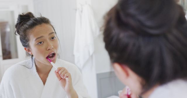 Woman brushing teeth in bathroom mirror wearing white robe - Download Free Stock Images Pikwizard.com