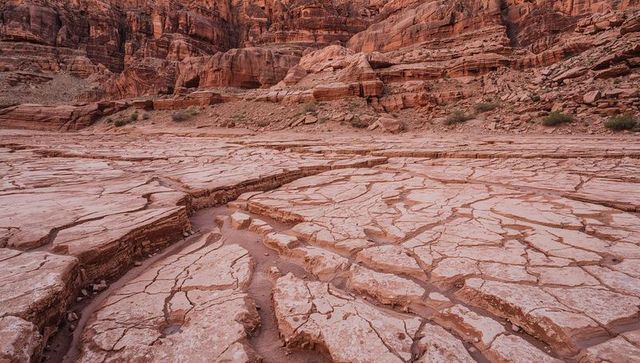 Cracked sandstone canyon floor revealing deep erosion channels and layered red rock cliffs