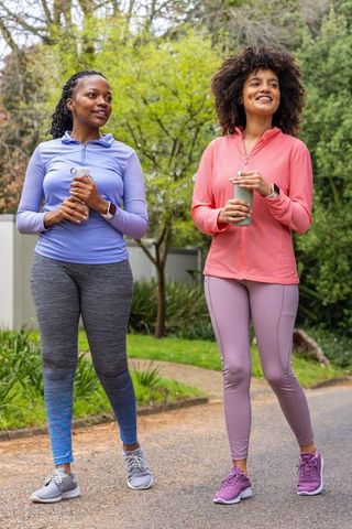 Two african american women walking in park holding reusable bottles wearing activewear