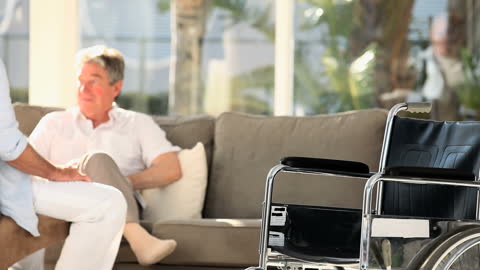 Elderly Man Conversing on Sofa with Wheelchair Foreground