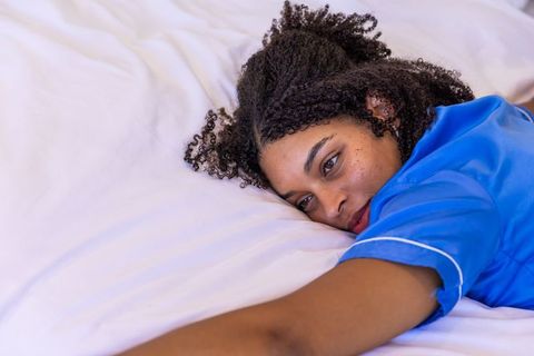 Relaxing african american woman resting on white sheets in blue pajamas, cozy closeup