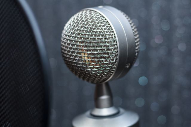 This close-up of a professional microphone with a blurred background is perfect for websites or articles related to audio recording, podcasting, voiceover work, and music production. The metallic and modern design makes it ideal for showcasing high-quality sound equipment. Can be used in promotional materials, blogs on audio tech, music production courses, or social media posts targeting audio industry enthusiasts.
