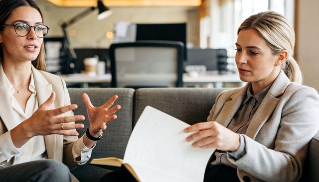 Two businesswomen discussing documents and strategy on modern office sofa during meeting