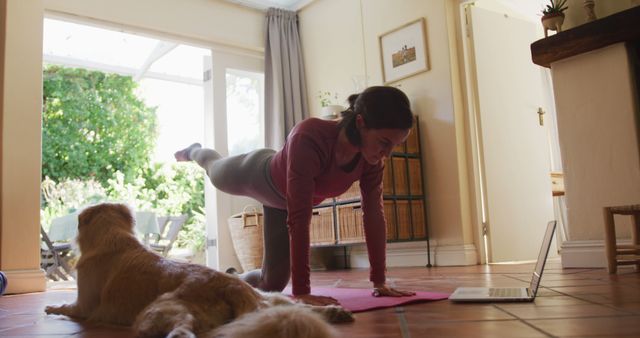Woman practicing yoga at home with her dog nearby. She is watching an online class on her laptop. Ideal for promoting home fitness routines, work-life balance, and the importance of staying active indoors. Suitable for content related to health, wellness, and pet companionship.