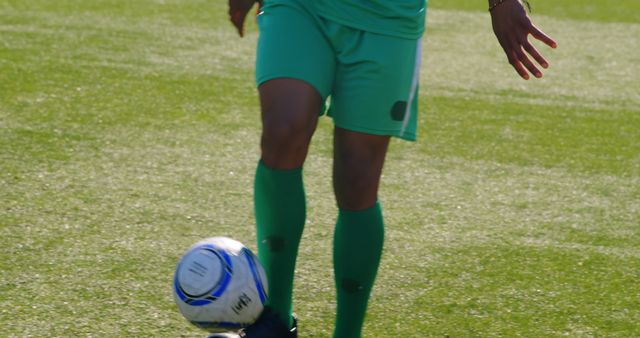A soccer player in a green uniform is dribbling a ball on a grass field. Use this for sports-related content, soccer training guides, or advertisements targeting athletes and sports enthusiasts.