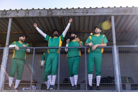 Cricket players celebrating on pavilion balcony wearing green and yellow team uniforms