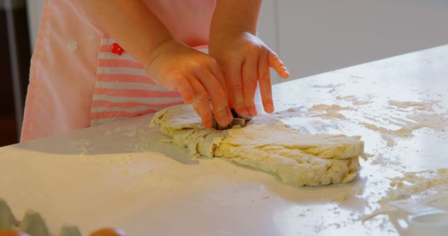 Child enjoying baking activity, using cookie cutter to shape dough into biscuits. Perfect for themes around home baking, family activities, child development, and culinary education.