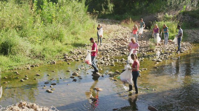 Group of diverse volunteers working together to clean up rubbish along a river in the countryside. Scene highlights teamwork and dedication to environmental conservation and social responsibility. Ideal for illustrating concepts of community service, eco-friendly initiatives, and volunteer work. Suitable for use in articles, blogs, and educational materials promoting environmental advocacy and volunteer opportunities.