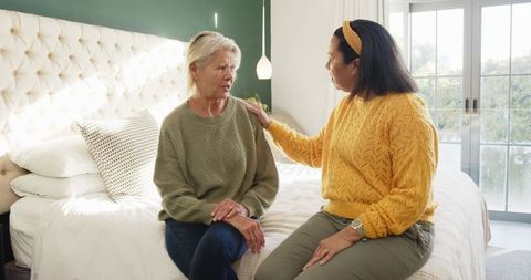 Diverse Female Caregiver Comforting Senior Client in Cozy Bedroom
