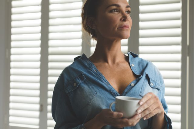 Thoughtful woman standing in living room while having coffee in a comfortable home