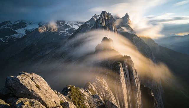 Golden sunrise over jagged alpine ridge with mist flowing across rocky peaks