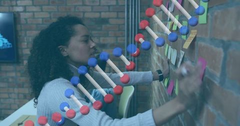 Woman writing sticky notes while brainstorming with DNA data overlay in creative coworking space