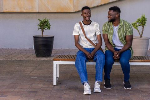 Two black men sitting on bench in urban courtyard smiling and talking, casual friendship