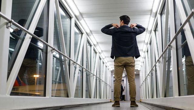 Business traveler adjusting blazer in glass jetway with reflections and leading lines