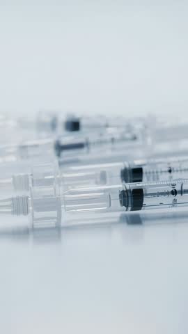 Vertical clinical video showing syringe and vial coming into focus on reflective tray