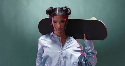 Stylish woman with skateboard in teal studio