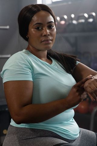 Confident african american woman resting on gym bench checking smartwatch after workout
