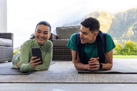 Young couple sharing workout routine on covered patio, checking phone and smiling