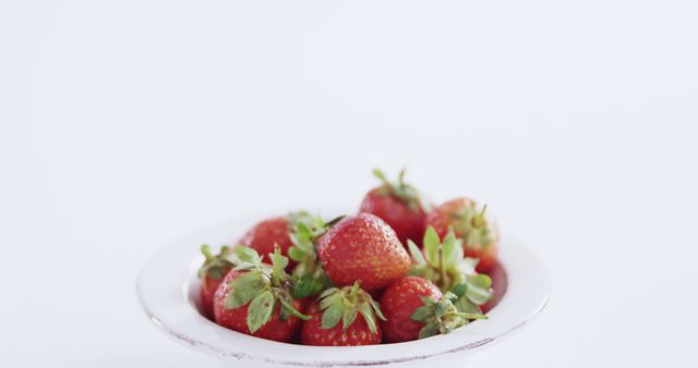 A plate of fresh strawberries is presented against a clean white background, with copy space. Vibrant red berries offer a visual appeal that suggests health and freshness.