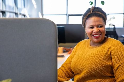 Smiling african american woman working at desk in modern office wearing mustard sweater