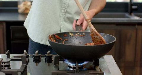 Man Cooking Carrot Strips in Wok on Gas Stove