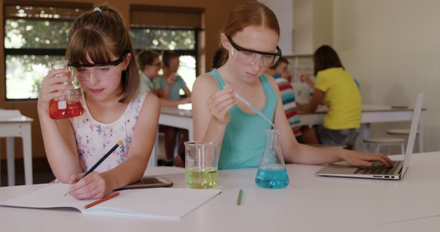 Focused caucasian schoolgirls doing experiment and making notes in elementary school chemistry class. Chemistry, experiment, science, childhood, education, learning and elementary school, unaltered.