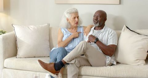 Senior Diverse Couple Sitting on Sofa Sharing a Light Moment Together