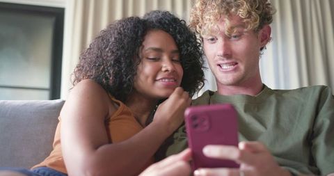 Young couple lounging on sofa sharing smartphone, smiling and scrolling through content