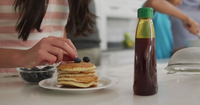 Hand Decorating Pancakes with Blueberries and Syrup Bottle on Kitchen Counter - Download Free Stock Images Pikwizard.com