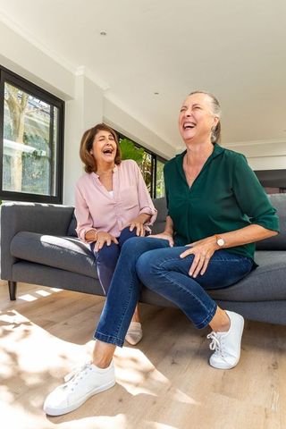 Senior and Adult Female Friends Laughing in Bright Living Room