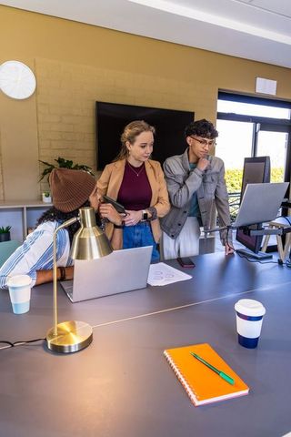 Young diverse team collaborating around modern conference table using laptops and smartphones