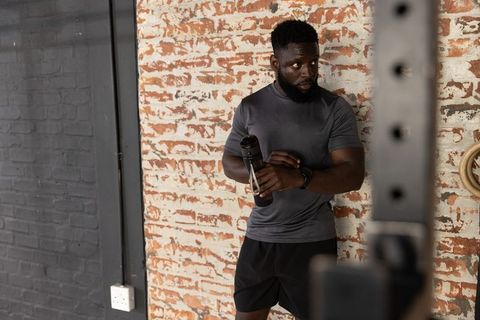 Focused african american athlete resting with shaker bottle against brick wall in gym