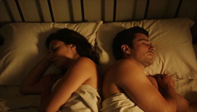 Couple sleeping back-to-back in warm bedroom glow intimate nighttime rest and quiet tension