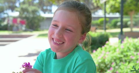 Preteen girl smiling and holding purple flower while relaxing outdoors in sunny park