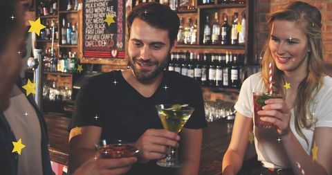 Friends enjoying cocktails at cozy bar, smiling and chatting while toasting drinks