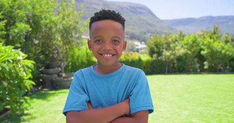 Smiling african american boy standing arms crossed in sunny backyard with fountain